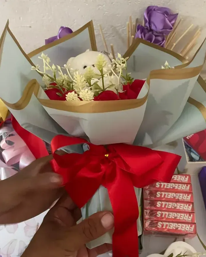 Rosas artificiais vermelhas e brancas com embalagem clara, bordas douradas e laço vermelho.