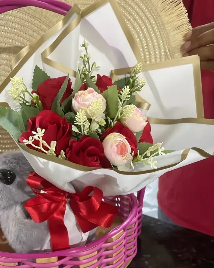 Rosas artificiais vermelhas e brancas com folhagens, embalagem clara e laço vermelho.
