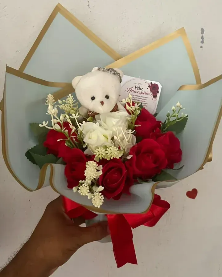 Rosas artificiais vermelhas e brancas com ursinho, embalagem clara e laço vermelho.